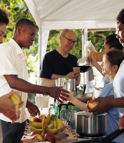 Diverse group of female volunteers donate free food to the poor and homeless people. Voluntary ladies offer refreshment and aid to those in need supporting a food drive for a non-profit organization.